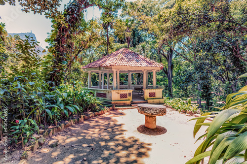The exterior of a gazebo structure on a paved path in a tropical garden on a sunny day.