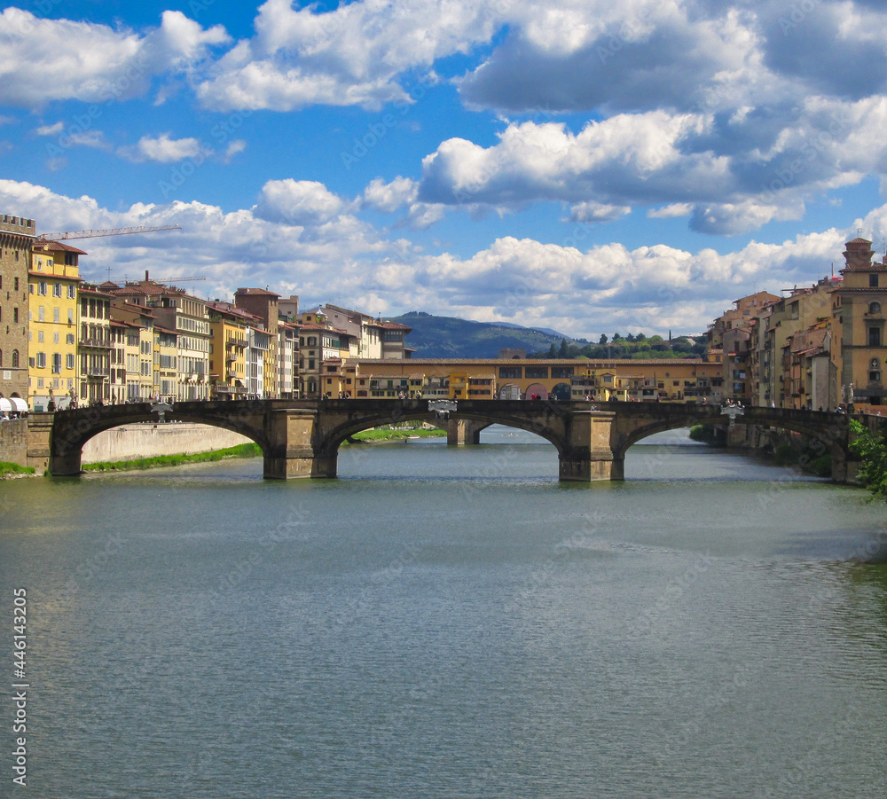 Medieval Ponte Vecchio bridge over the Arno river under a blue cloudy sky in Florence