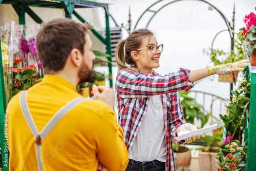 Smiling female entrepreneur offering flowers to a customer. Greenhouse interior. © dusanpetkovic1