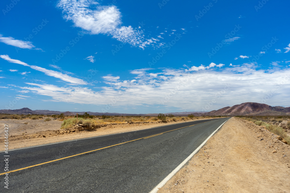 Long Mojave Desert road with cloudy blue sky