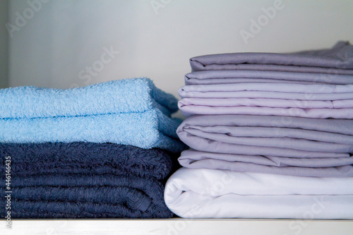 Folded bedding and fresh clean cotton bath towels on gray background, closeup. High quality photo of colorfull pastel home textile