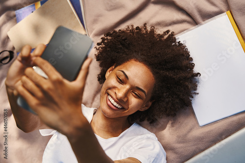 Gladsome pretty lady smiling tocamera while lying on a blanket and taking photos photo