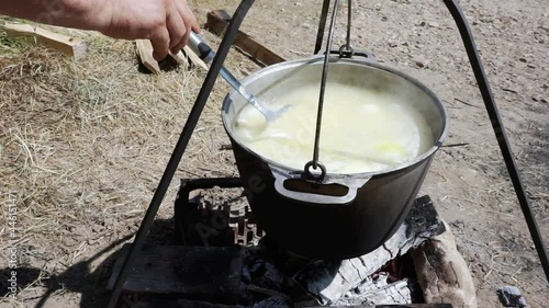 Close-up of boiling fish soup in a saucepan over a fire during a hike, a tourist interferes with the ear with a slotted spoon photo