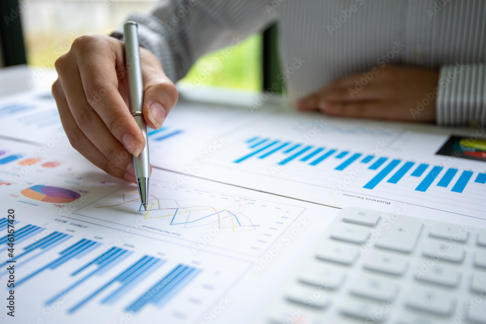 Close up of Hand business woman holding pen pointing on chart summary report and calculate finance. Close up of Hand business woman holding pen pointing on chart summary report and calculate finance.