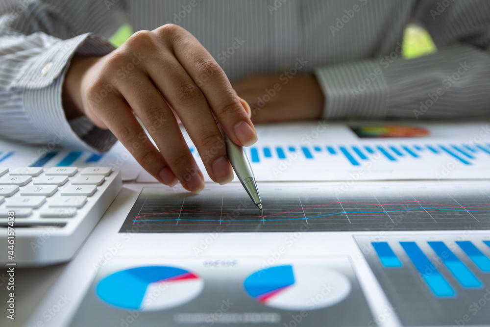 Close up of Hand business woman holding pen pointing on chart summary report and calculate finance. Close up of Hand business woman holding pen pointing on chart summary report and calculate finance.