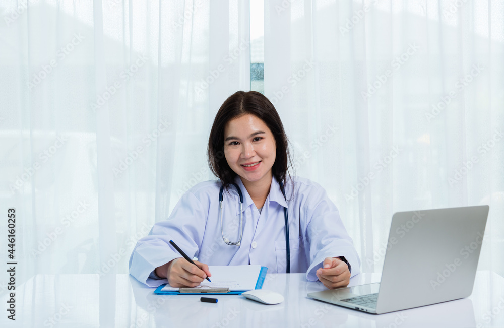 Asian doctor young beautiful woman smiling using working with a laptop computer and her writing something on paperwork or clipboard white paper at hospital desk office, Healthcare medical concept Asian doctor young beautiful woman smiling using working with a laptop computer and her writing something on paperwork or clipboard white paper at hospital desk office, Healthcare medical concept