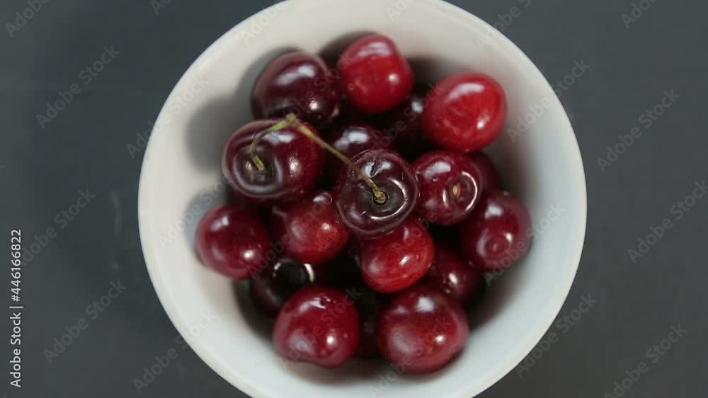 Ripe juicy cherries in a white bowl on a black background rotate in a circle Ripe juicy cherries in a white bowl on a black background rotate in a circle