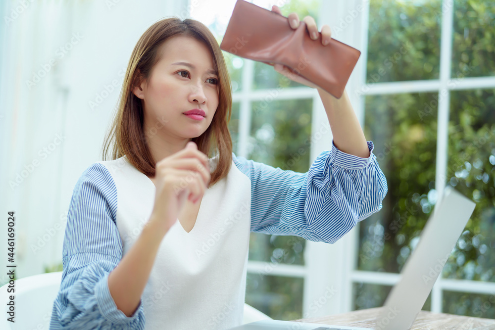 Half-body portrait of an Asian woman in a white shirt sitting in a bakery examining her purse for money with a stressed, unhappy face.