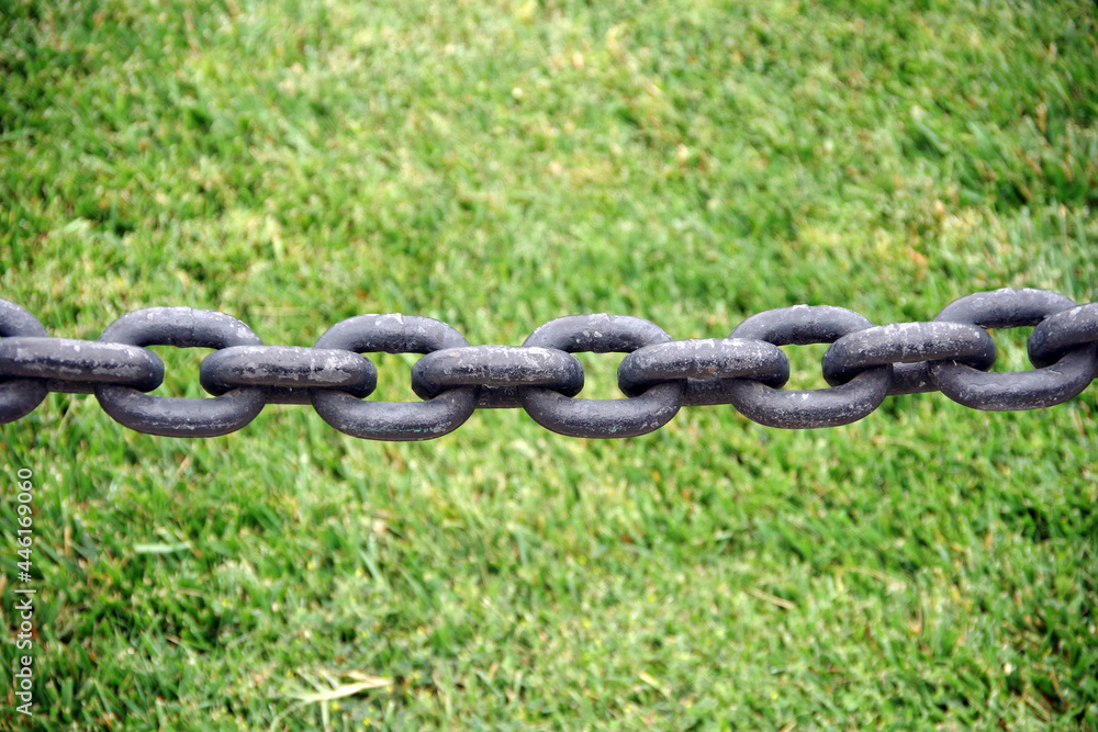 Close-up view of a segment of a heavy black iron chain closing off a grassy park area Close-up view of a segment of a heavy black iron chain closing off a grassy park area