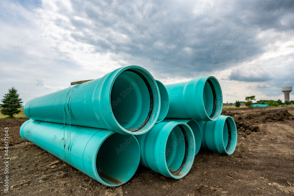 Stacked water main pipe with bell fitting next to an exposed trench for installation Stacked water main pipe with bell fitting next to an exposed trench for installation