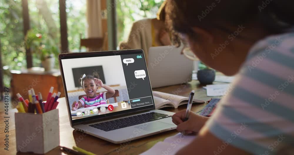 Schoolgirl using laptop for online lesson at home, with school friend and web chat on screen