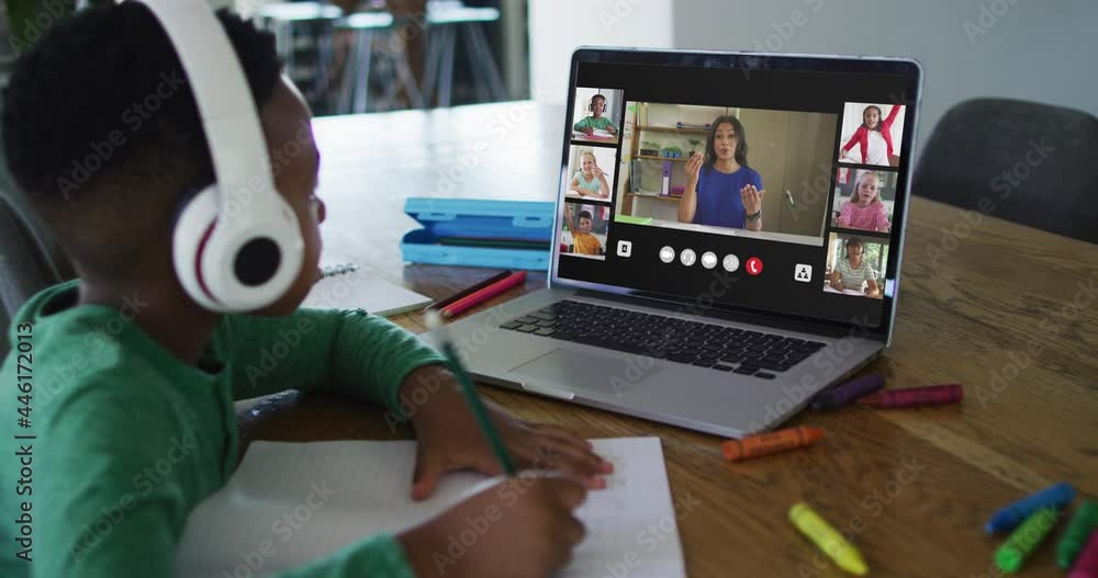 Schoolboy using laptop for online lesson at home, with diverse teacher and class on screen