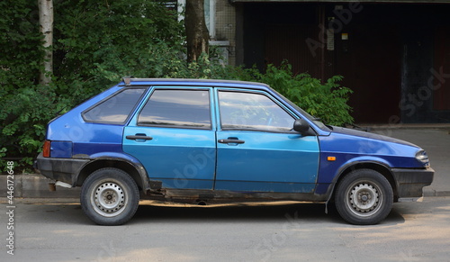 An old rusty dark-blue car with light-blue doors on the road, Dybenko Street, St. Petersburg, Russia, June 2021
