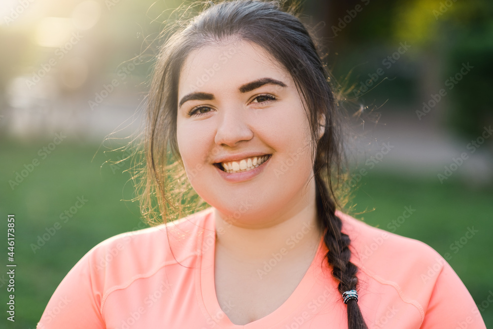 Overweight woman. Imperfect body. Plus size beauty. Happy lifestyle. Portrait of cheerful young obese plus size lady smiling outdoors in defocused green park landscape. Overweight woman. Imperfect body. Plus size beauty. Happy lifestyle. Portrait of cheerful young obese plus size lady smiling outdoors in defocused green park landscape.