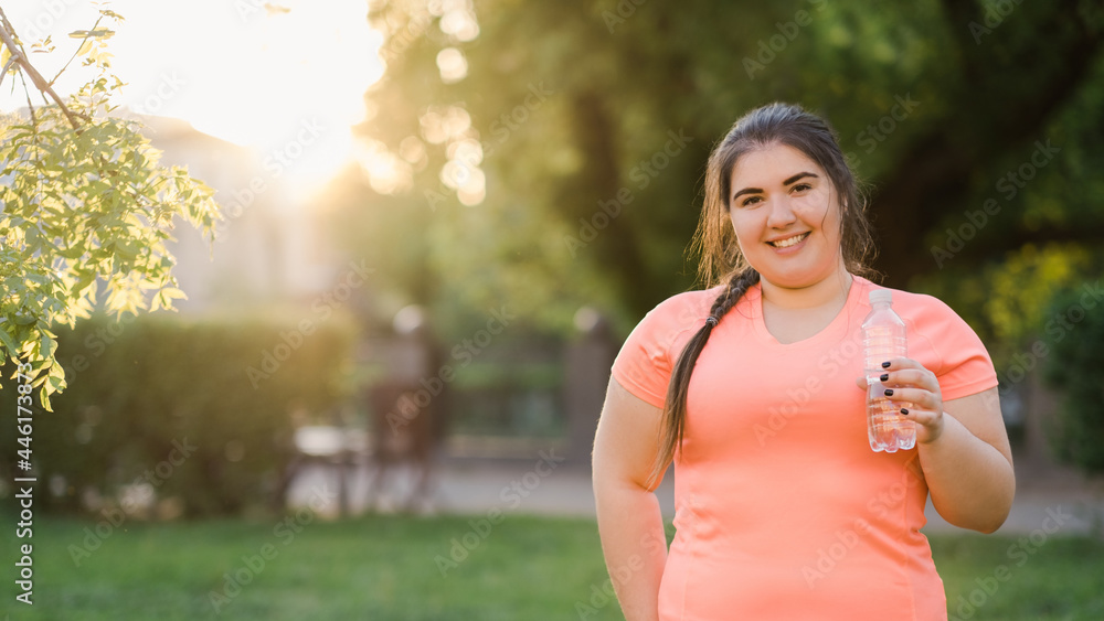 Water hydration. Weight loss diet. Body positive. Healthy lifestyle. Happy smiling young obese overweight woman holding bottle with clear liquid in defocused empty space park.