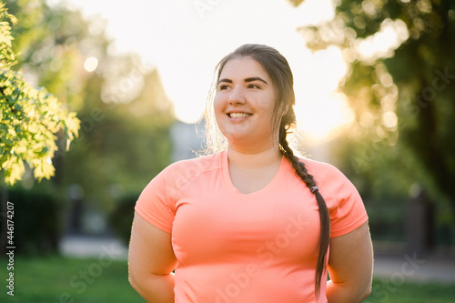 Obesity people. Plus size woman. Body positive. Weight confidence. Joyful chubby young obese overweight girl smiling outdoors in defocused green park street landscape. photo