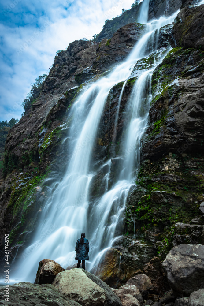 Fototapeta premium waterfall white water stream falling from mountains with girl standing nearby at day long exposure