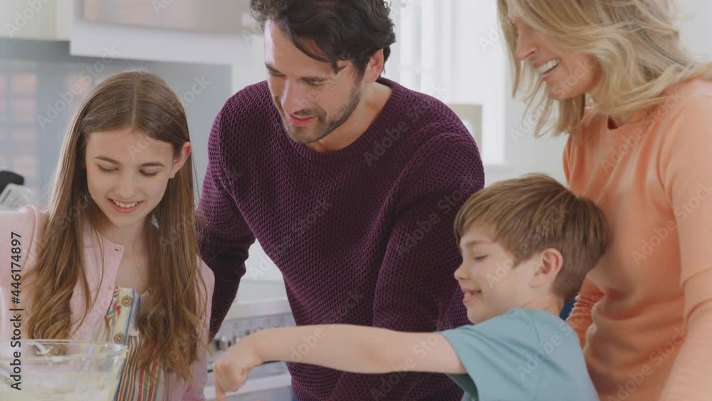 Family With Two Children In Kitchen At Home Having Fun Baking Cakes Together