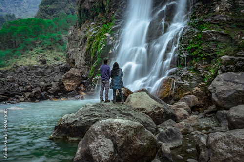 couple standing at rock in front of waterfall water stream falling from mountains long exposure