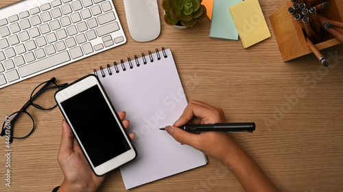 Female Han holding mobile phone and making note on notebook.