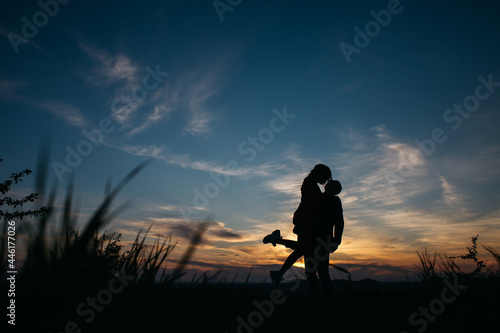 silhouette of a couple at sunset. guy holding a girl in his arms.