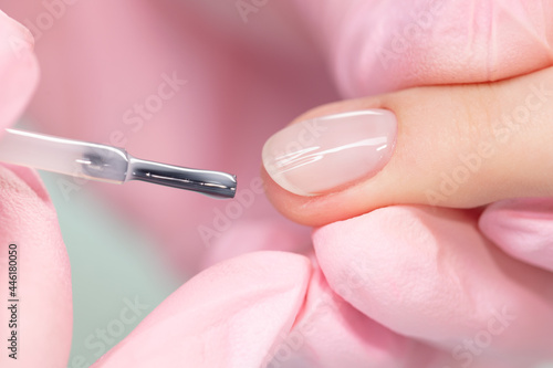 Close up process of applying transparent varnish. Woman in salon receiving manicure by nail beautician.Сlear nail polish and brush, macro. Shallow depth of field