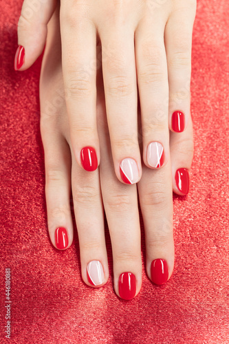Female hands with new manicure. Hands with pink and red nail polish on a red background. Care for woman hands. Woman in salon receiving manicure by nail beautician. Selective focus