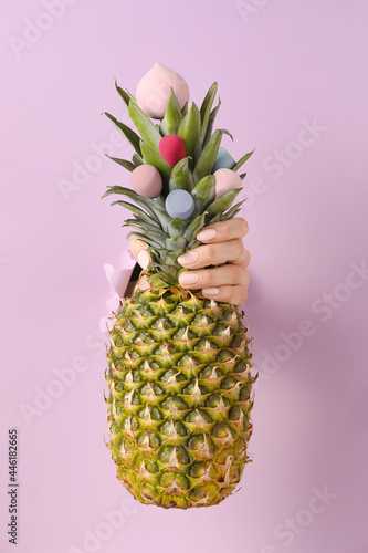 Female hand with fresh pineapple and makeup sponges visible through hole in color paper