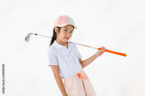 Portrait close up isolated studio shot of pretty cute long hair little Asian golfer in sport uniform and colorful cap stand posing holding golf club driver across shoulder in front white background