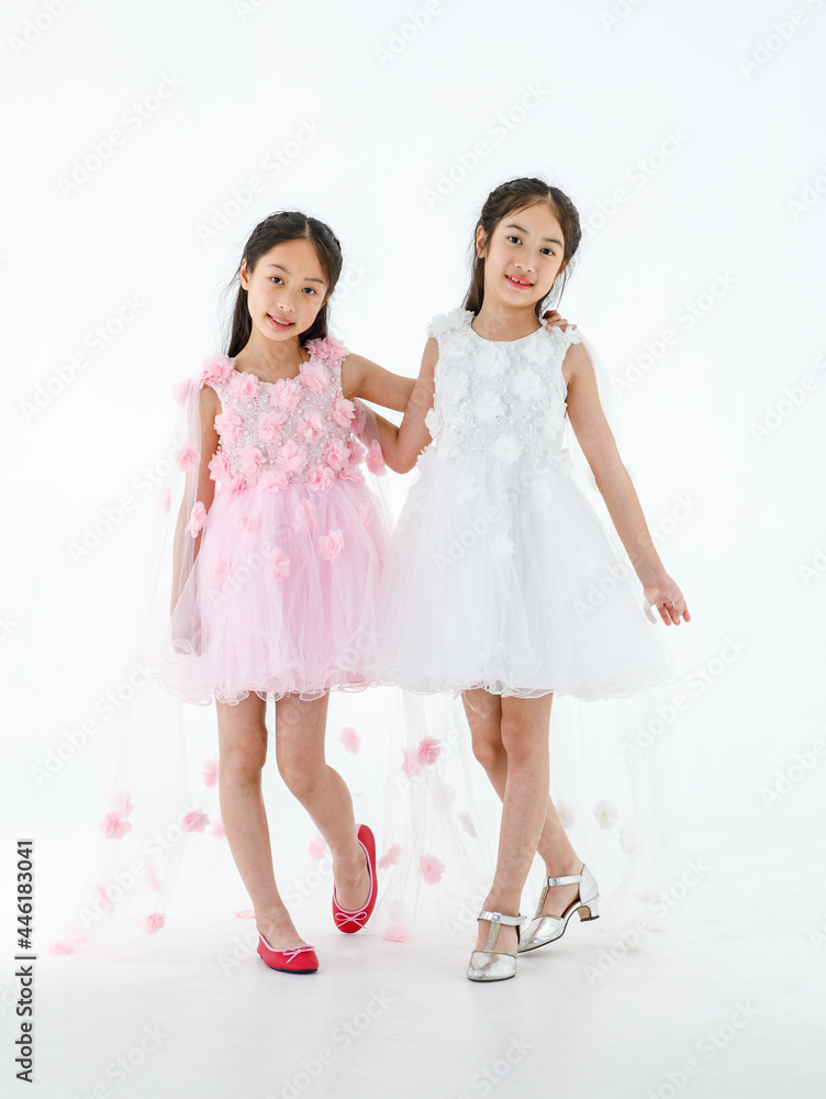 Portrait isolated studio shot of two little Asian ballerina kids in pink and white beautiful roses flowers ballet dress red shoes and high heels smile look at camera together Portrait isolated studio shot of two little Asian ballerina kids in pink and white beautiful roses flowers ballet dress red shoes and high heels smile look at camera together