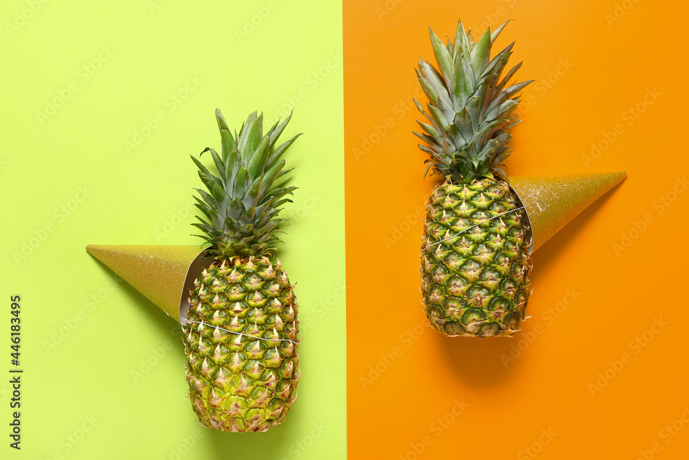 Fresh pineapples in party hats on color  background