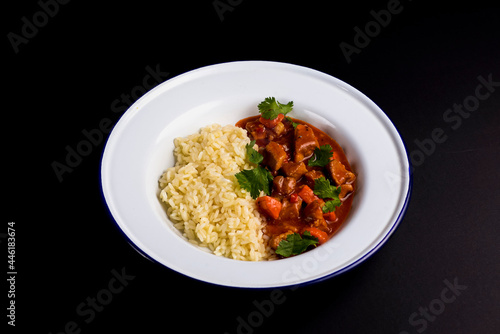 Chicken gravy with rice served in a white plate over black background.