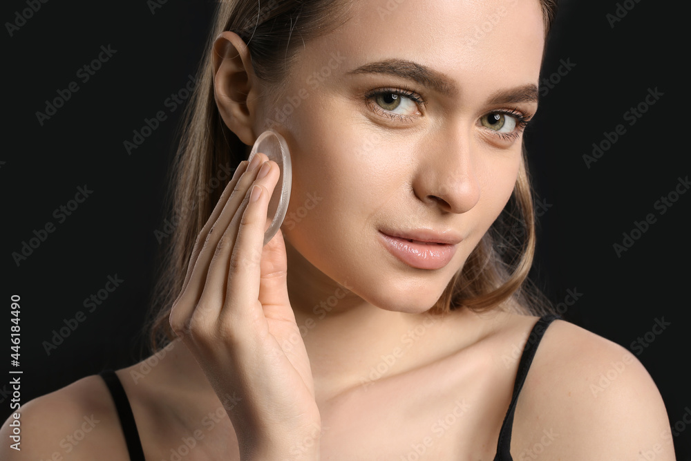 Beautiful young woman with makeup sponge on dark background