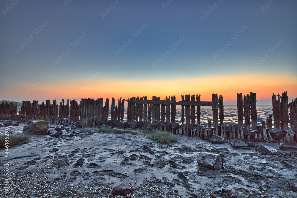 View of the Wadden Sea during sunset, at low tide. Wooden posts as a silhouette in the mud. UNESCO. Wadden Sea World Heritage