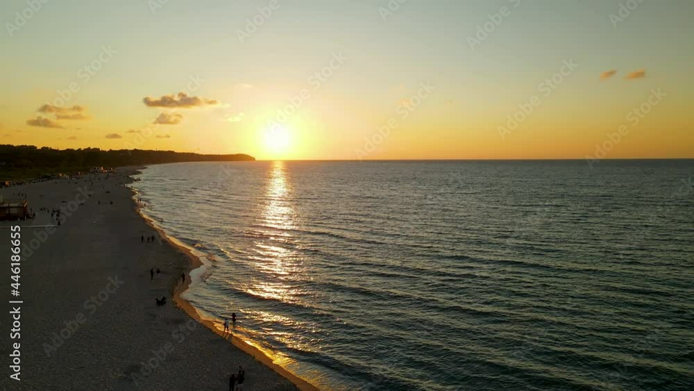 Aerial flyover coastline of Baltic Sea during golden hour with walking people along shore of Coastline. Wladyslawowo Bay in Poland. Aerial flyover coastline of Baltic Sea during golden hour with walking people along shore of Coastline. Wladyslawowo Bay in Poland.