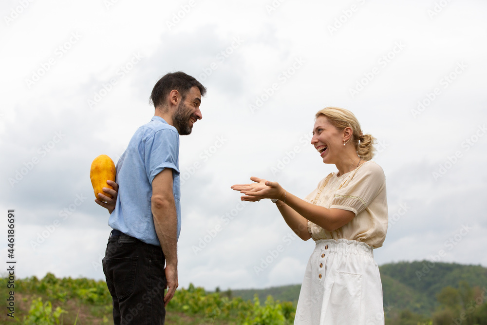 Caucasian man holding papaya behind his back,woman in front of him, relationship, couple, vegetarian Caucasian man holding papaya behind his back,woman in front of him, relationship, couple, vegetarian