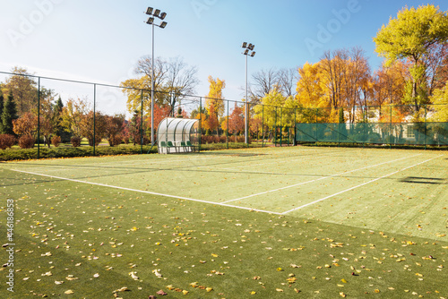 Tennis court in the autumn park. The playground is covered with fallen leaves.