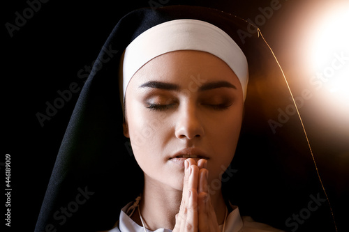 Young praying nun on dark b...