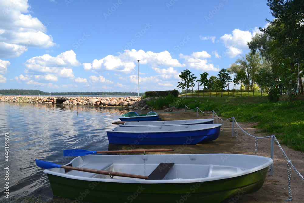 Boats near to the stone pier on the shore of the lake in sunny summer day. Beautiful landscape. Wallpaper. Horizontal view. Eco-tourism.