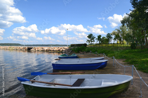 Boats near to the stone pier on the shore of the lake in sunny summer day. Beautiful landscape. Wallpaper. Horizontal view. Eco-tourism.