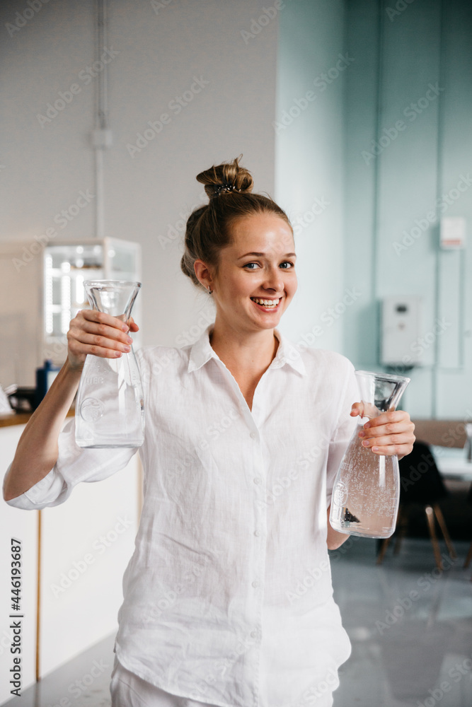 Attractive young woman in white casual outfit holding two glass reusable bottles with clear water. Healthy life and water consumption rate concept Attractive young woman in white casual outfit holding two glass reusable bottles with clear water. Healthy life and water consumption rate concept