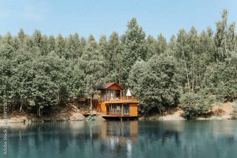 Modern aesthetic wooden house on the lake. Exterior of a country house, cottage on the water near the forest, summer day.