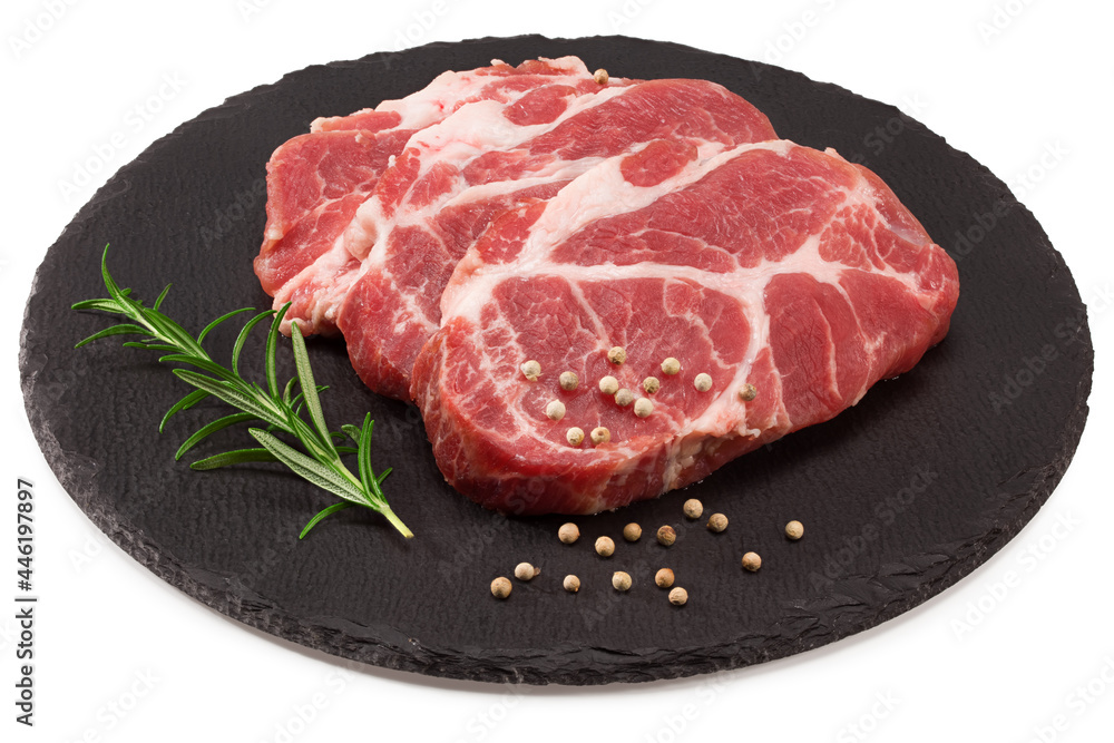 raw pork meat with rosemar, tomato and peppercorn on black round stone plate isolated on white background. Clipping path and full depth of field