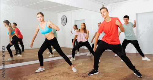 Cheerful teens practicing dance, stretching with young female trainer in dance hall..