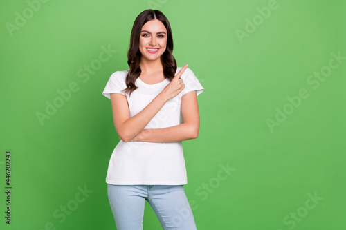 Photo of optimistic brunette millennial lady point empty space wear t-shirt jeans isolated on green color background