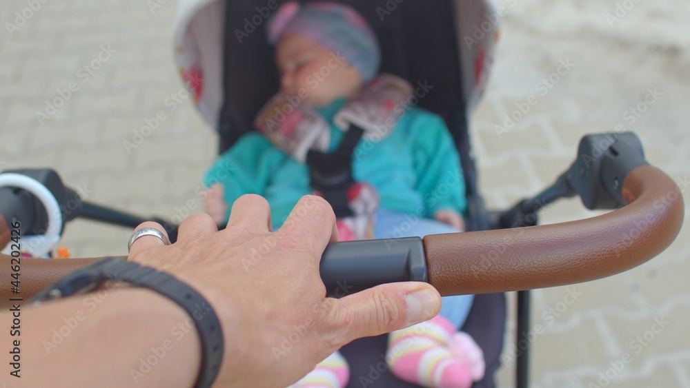 Father's hand holds the handle of a stroller with a baby boy. He rolls along the sidewalk. Transportation of a child around the city for a walk. Shaking the camera.