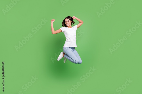 Full body photo of funky brunette young lady jump wear t-shirt jeans isolated on green color background