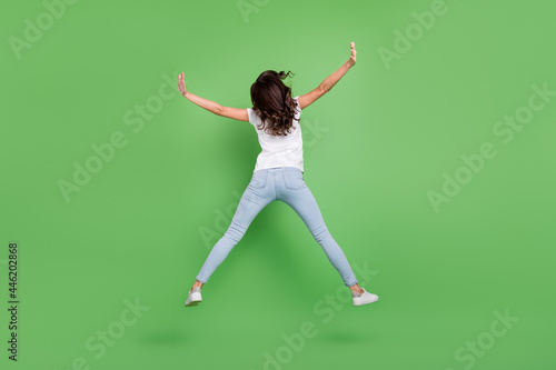 Full body back photo of cool brunette young lady jump wear t-shirt jeans isolated on green color background