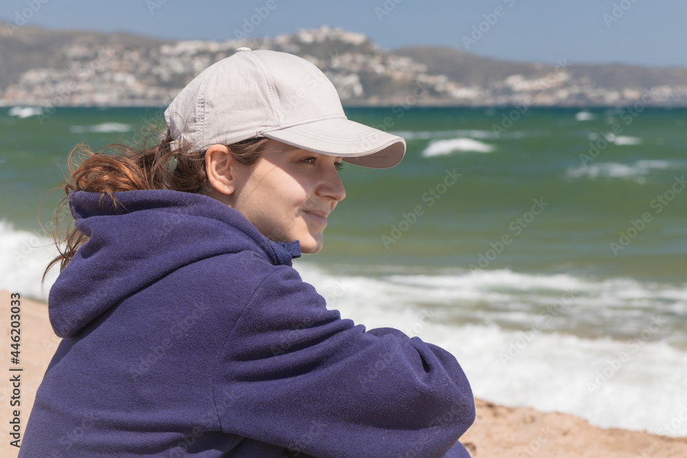 Natural portrait of a young caucasian woman, no retouching skin, no color correction. Girl outdoor portrait on a ocean background, brunette in baseball cap, naturalness