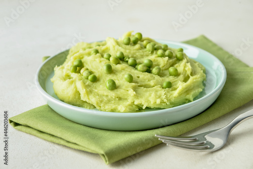 Plate with mashed potatoes, green peas and fork on light background